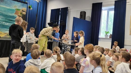grupa dzieci oglądających przedstawienie teatralne, kilkoro z nich trzyma z aktorem siatkę rybacką