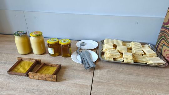 stół na którym  znajdują się słoiki z miodem, talerze oraz pokrojone wafle