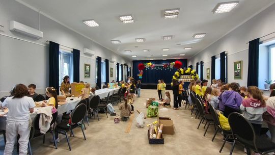 grupa uczniów siedzących przy stolikach, wykonują prace plastyczne, w tle sala widowiskowa