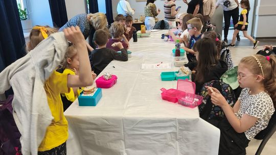 grupa uczniów siedzących przy stolikach, wykonują prace plastyczne, w tle sala widowiskowa