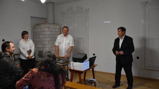 W sali Starej Plebanii w Fajsławicach odbywa się spotkanie autorskie z Januszem Szwajewskim. Przed uczestnikami stoją organizatorzy wydarzenia oraz przedstawiciel samorządu, który przemawia do zgromadzonych gości.