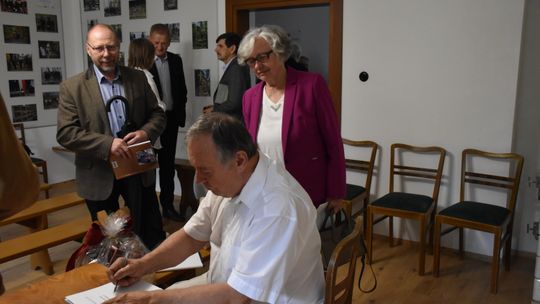 Autor składający autograf na swojej książce, wokół uczestnicy spotkania promującego książkę.