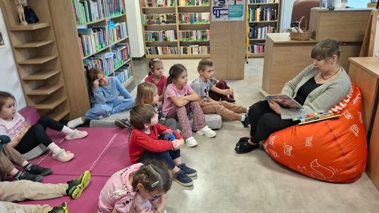 Dzieci siedzą w bibliotece i słuchają fragmentu książki „Kto tam jest? W oceanie”, poznając zwierzęta żyjące w oceanie. Siedząca na pufie bibliotekarka czyta im książkę i pokazuje ilustracje.