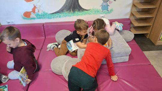 Dzieci siedzą na pufach i przeglądają książeczki.